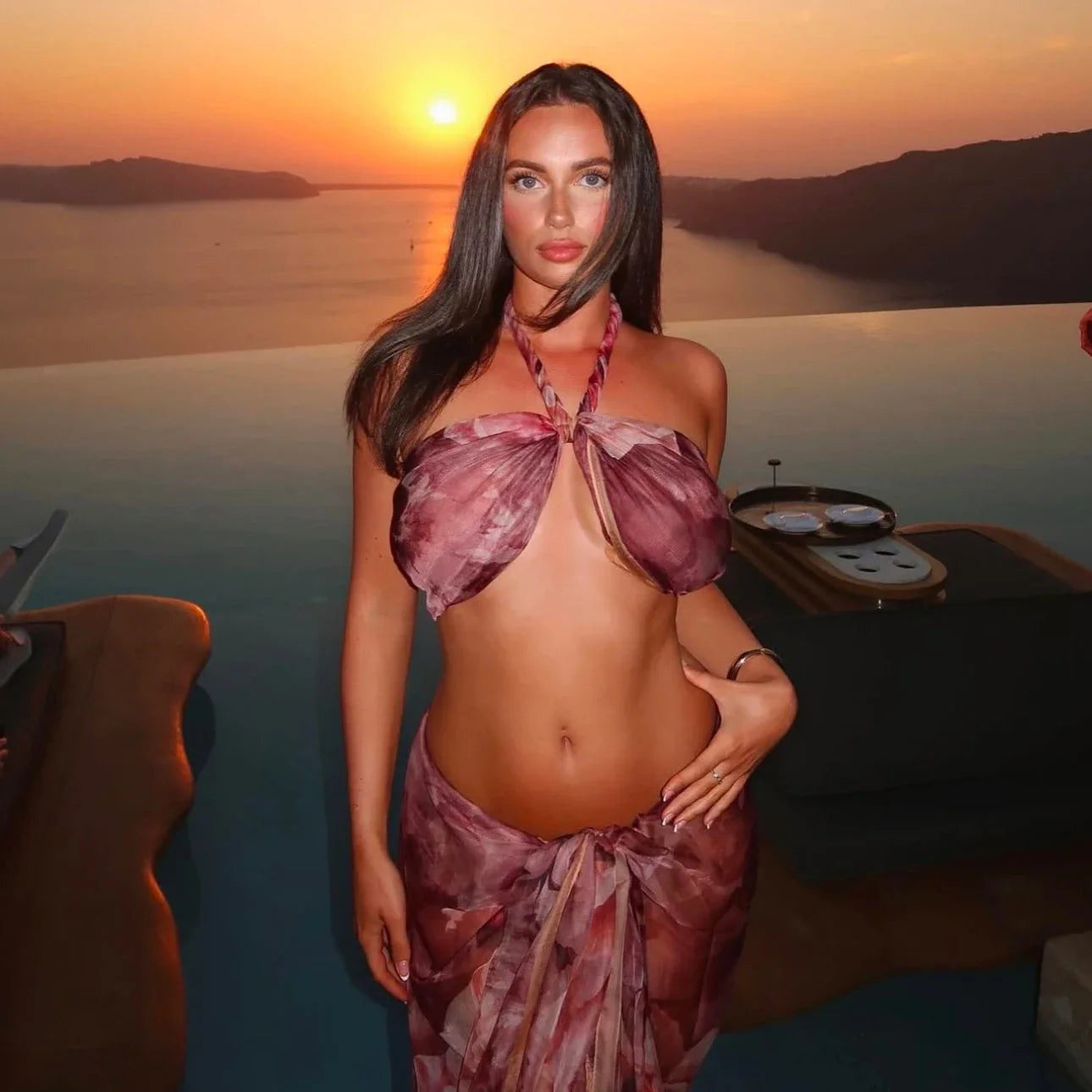 Woman in a floral dress standing by a sunset over water